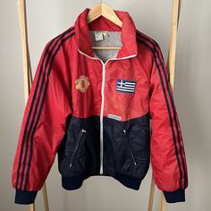 This vintage Adidas Manchester United wind breaker is a rare and highly collectable item.  For all the football fans this jacket is in fabulous condition with the Manchester United Football Club emblem on the front.  There are two badges on the other side - an Adidas one and another one - the Greek flag - looks like its been added by the owner and hand stitched on.  If you hate this it look easy to take off as its been just hand stitched.   All zips work perfectly.  There are no stain or holes i Retro Red Track Jacket For Outdoor, Red Retro Track Jacket For Outdoor, Vintage Red Track Jacket For Outdoor, Vintage Red Sports Outerwear, Vintage Red Outerwear For Sports, Retro Red Sports Windbreaker, Retro Red Windbreaker For Sports, Vintage Red Windbreaker For Streetwear, Vintage Winter Track Jacket For Sports Events