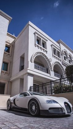 a white bugatti parked in front of a large building with balconies