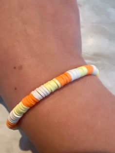 an orange, white and yellow bracelet on someone's arm in the sand at the beach