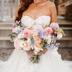 a woman holding a bouquet of flowers in her hands and wearing a wedding dress with lace