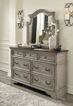 a dresser with a mirror on top of it next to a rug and wall sconces