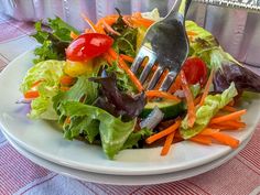 a salad with carrots, lettuce and cherry tomatoes on it is being held by a fork