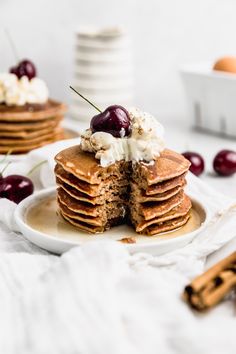 a stack of pancakes topped with whipped cream and cherries on a white plate next to cinnamon sticks