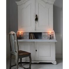 an old white cabinet with candles on it and a chair next to it in front of it