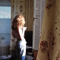 a woman standing in front of a window with her back turned to the camera and looking out