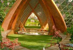 a large wooden structure sitting in the middle of a lush green field with flowers and trees