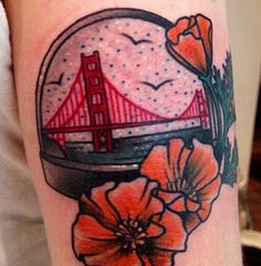 a close up of a tattoo with flowers and a bridge in the background