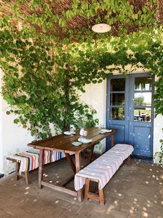 a wooden table sitting under a tree next to a blue door