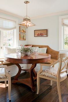 a dining room table with two chairs and a bench in front of the window,