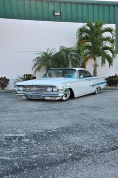 an old white car parked in front of a building with palm trees on the side