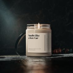 a candle sitting on top of a wooden table next to a black mug with the words smells like a new car written on it