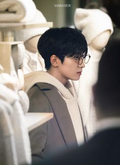 a young man with glasses standing in front of clothes