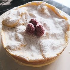 two raspberries sit on top of a powdered pastry