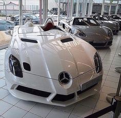 several cars are parked in a showroom with white tile flooring and large windows