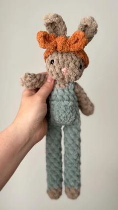 a hand holding a small crocheted bunny with an orange bow on its head