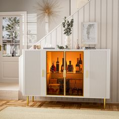 a white cabinet with bottles in it sitting on top of a wooden floor next to a stair case