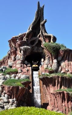 the entrance to an amusement park with water coming out of it's mouth and trees growing on top