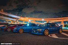 three cars parked in a parking lot at night with lights shining on the building behind them