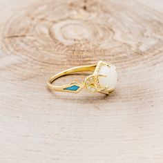 a gold ring with an opal and turquoise stone in the center on a wooden surface