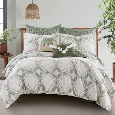 a bed with green and white comforters in a room next to a plant on the floor