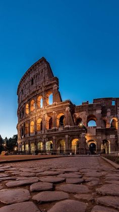 the roman colossion at night with its lights on and cobblestones in front