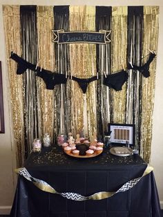 a black table topped with cupcakes and cake next to a gold drapes