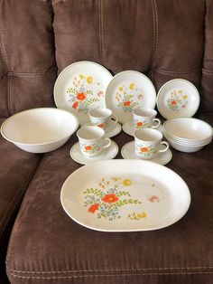 there are many dishes and cups on the couch with one plate in front of them