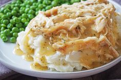 a white plate topped with mashed potatoes covered in gravy and green peas