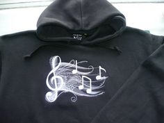 "Musician Hoodie - stave with treble clef and notes.  Beautiful lacy embroidered Design on the FRONT of a Hoodie. BLACK garment with design in WHITE MEDIUM Embroidered Design (approx. design size up to 200mm x 200mm) on the FRONT of a HEAVY Hoodie. Sizes XS 34\" S 36\" M 40\" L 44\" XL 48\" 2XL 52\" 3XL 56\"  WASHING INSTRUCTIONS - Machine wash 30o. Do not bleach. Tumble dry low heat. Low iron. Do not dry clean. OTHER OPTIONS - This design is also available on a Heavy SWEATER, or Cotton Canvas Messenger Bag (approx. design size 200mm x 200mm). FULL GARMENT SPEC - Our Heavy Men's Pullover Hoodie, with it's simple and stylish classic fit is an essential for any hoodie lover. * 80% Ringspun cotton, 20% Polyester. Made from cotton faced fabric Twin-needle stitching detailing. * Double fabric h Hip Hop Cotton Hoodie For Concert, Cotton Hip Hop Hoodie For Concerts, Winter Concert Hooded Sweatshirt, Concert Cotton Hooded Sweatshirt, Cotton Hooded Sweatshirt For Concert, Winter Cotton Hoodie With Band Logo, Cotton Hoodie With Band Logo, Garment Manufacturing, Heavy Sweaters