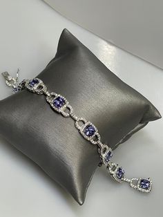 STUNNING TANZANITE AND DIAMOND BRACELET This is one amazing piece! From our fancy colored stone collection. An absolutely stunning tanzanite and diamond bracelet. Designed and made in 14 karat solid white gold. This stunner is the epitome of elegance! Bracelet consists of 8 square cushion cut blue tanzanites and 296 diamonds! The diamonds accent the four prong set tanzanite creating an initial halo yet cascading across the top of the links. A hidden box clasp with figure eight safety clasp keeps Formal Purple Sapphire Jewelry, Dazzling Tanzanite Jewelry With Diamond Accents, Dazzling Tanzanite Jewelry, Silver Tanzanite Bracelet In Fine Jewelry Style, Silver Tanzanite Bracelet Fine Jewelry, Formal Purple Cubic Zirconia Bracelets, Formal Blue Tanzanite Bracelets, Formal Purple Tanzanite Jewelry, Silver Tanzanite Bracelets For Formal Occasions