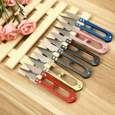 six different colored knives are on a wooden table next to some flowers and a pink rose