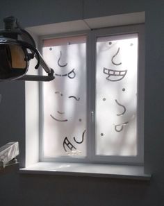 a window with faces drawn on it in front of a white wall and light coming through the window