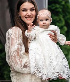 a woman holding a baby wearing a white dress and head piece with pearls on it