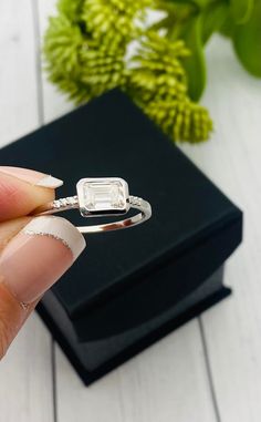 a woman's hand holding an engagement ring in front of a box with flowers