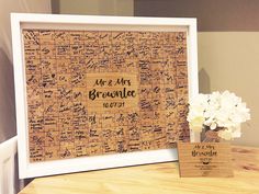 a wooden table topped with a vase filled with flowers next to a framed cork board