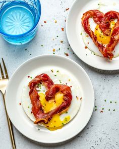 two white plates topped with eggs and bacon in the shape of a heart next to a fork