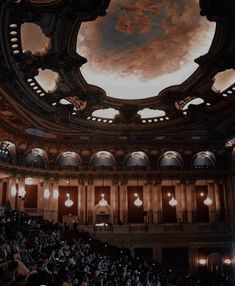 an auditorium filled with lots of people sitting in chairs and looking up at the ceiling