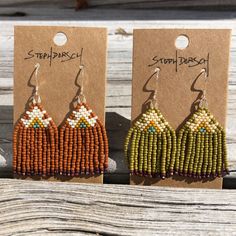 three seed beaded earrings are sitting on a wooden table