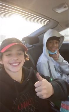 two people sitting in the back seat of a car with thumbs up and one person wearing a hoodie