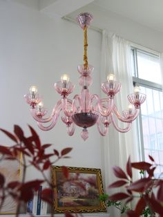 a pink chandelier hanging from the ceiling in front of a painting and window