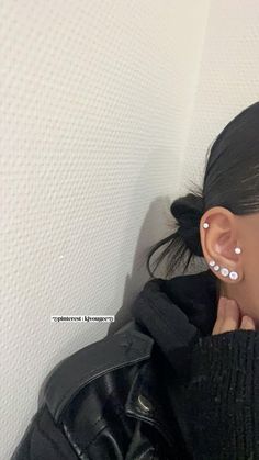 a close up of a person wearing ear piercings and a black jacket with a white wall in the background