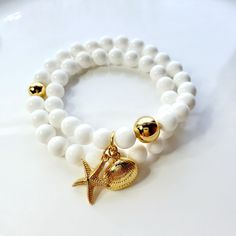 White shell bead wrap bracelet with gold seashore charms This beautiful bracelet is made with 8mm shell beads and 2 gold plated seashore charms and 2 round gold beads that wrap around your wrist twice and fit a 7.5-inch wrist which fits most and is an industry standard size. Gold Bracelet With Pearl Charm For Beach, Gold Beaded Bracelets With Starfish Charm As Gift, Gold Bracelet With Starfish Charm, Adjustable, Adjustable White Jewelry With Starfish Charm, White Starfish Charm Bracelet, Gold Charm Bracelet With Starfish For Beach, Adjustable Gold Charm Bracelet Ocean-inspired, Adjustable Gold Charm Bracelet With Starfish Charm, Gold Beaded Charm Bracelet For Beach