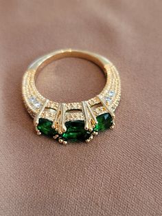 The ring is a 3 stone trilogy style with a one carat round emerald center stone and two .50 carat round emerald stones on each side.  There are .33 carat diamond accents on the band.  Stamped 14K. Green Three Stone Emerald Cut Emerald Ring, Green Three-stone Emerald-cut Emerald Ring, Three-stone Emerald Cut Green Emerald Ring, Green Emerald Cut Three Stone Emerald Ring, Formal Three Stone Emerald Cut Birthstone Ring, Formal Three-stone Emerald-cut Birthstone Ring, Emerald Cut Three Stone Birthstone Ring For Formal Occasions, Formal Emerald Cut Three Stone Birthstone Ring, Formal Emerald Three-stone Ring