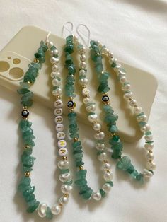 four necklaces with pearls and green beads on a white phone case next to a cell phone