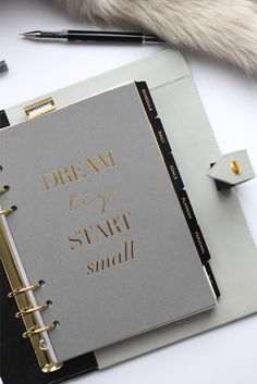 a notebook with gold writing on it and a pen next to it that says dream stay small