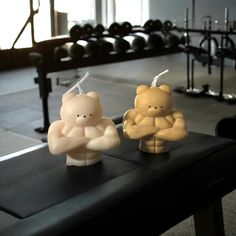 two small teddy bears sitting on top of a table in front of a rack of dumbbells