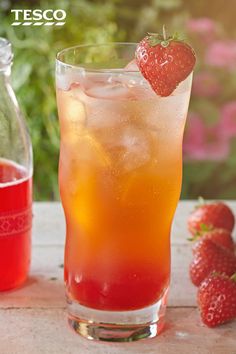 a glass filled with ice and strawberries next to a bottle full of tea on a table