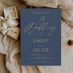 a blue wedding card with gold foil lettering on it, surrounded by rings and jewelry