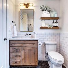 a white toilet sitting next to a wooden sink vanity in a bathroom under a mirror