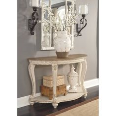 a white vase sitting on top of a wooden table next to a mirror and lamp